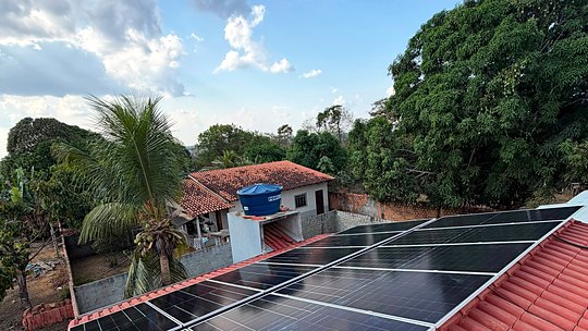 Módulos solares em telhado de residência cercada por vegetação